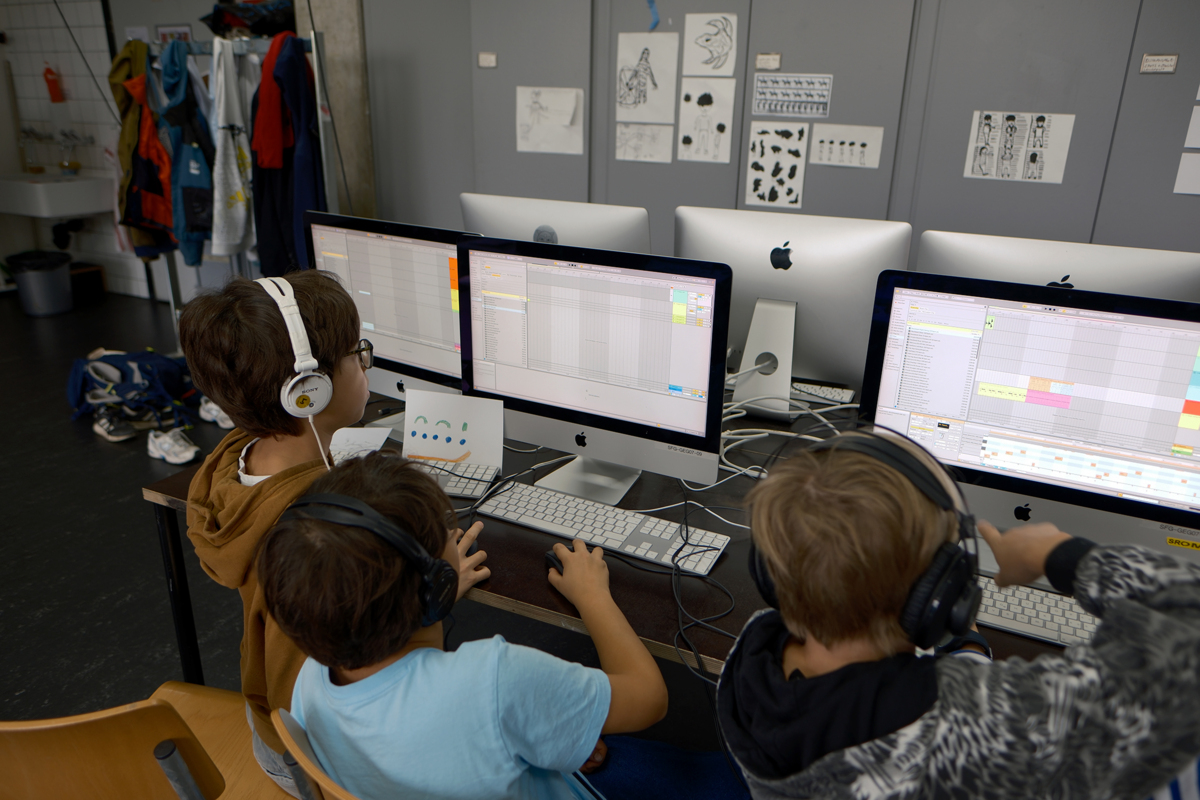 Kinder sitzen mit Kopfhörern an Computern und bearbeiten Video- und Tonspuren