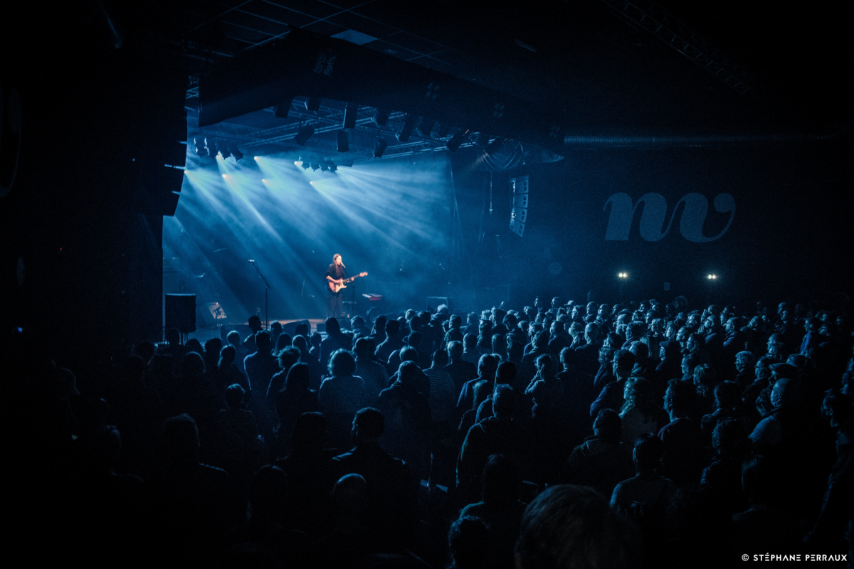 BARANY live auf der Bühne, Leadsängerin mit Gitarre in der Hand auf grosser Bühne vor Publikum in blauem Bühnenlicht