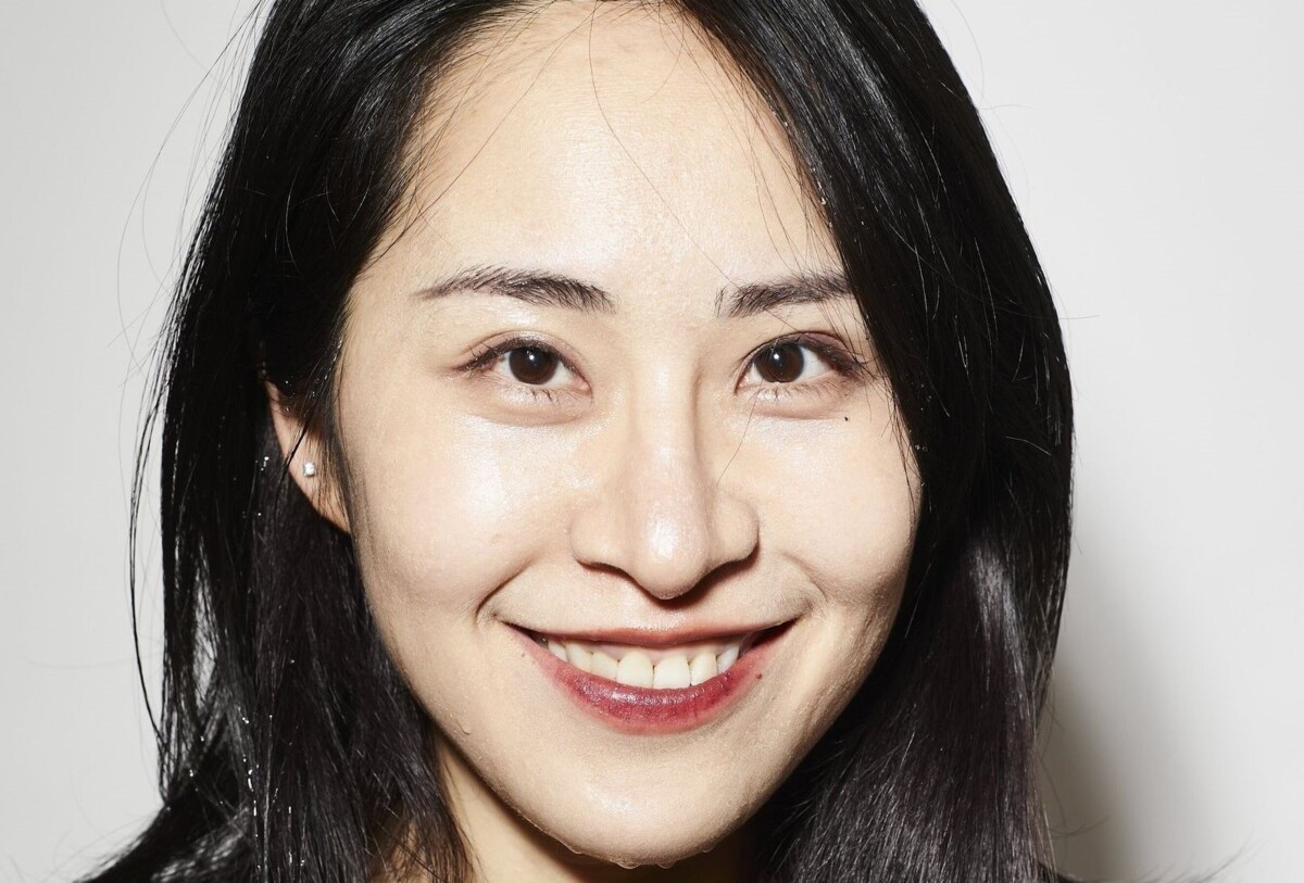 Porträt von Yi-Zhen Tsai, die in einem schwarzen Kleid vor einem weissen Hintergrund sympathisch in die Kamera lacht.