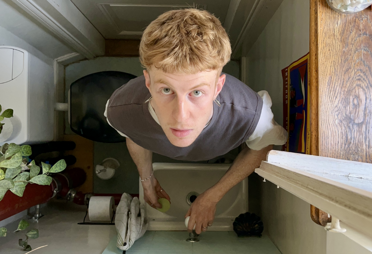 Anton Kiefer wird von oben fotographiert in einer Toilette, vor einem Abwaschbecken stehend und hoch in die Kamera schauend