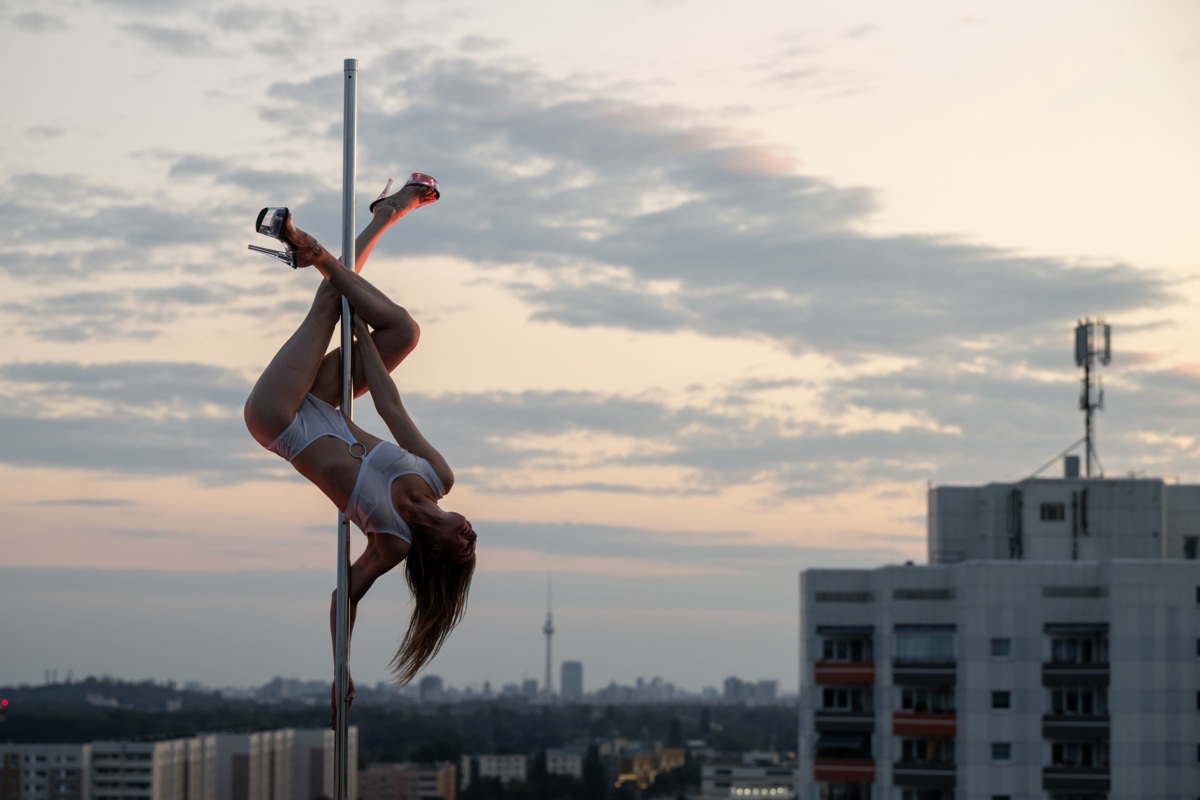 Frau an Pole Dance Stange mit einer Stadt im Hintergrund.