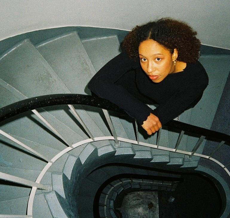 Foto von Emily Adomah von oben in pastelblauem Treppenhaus