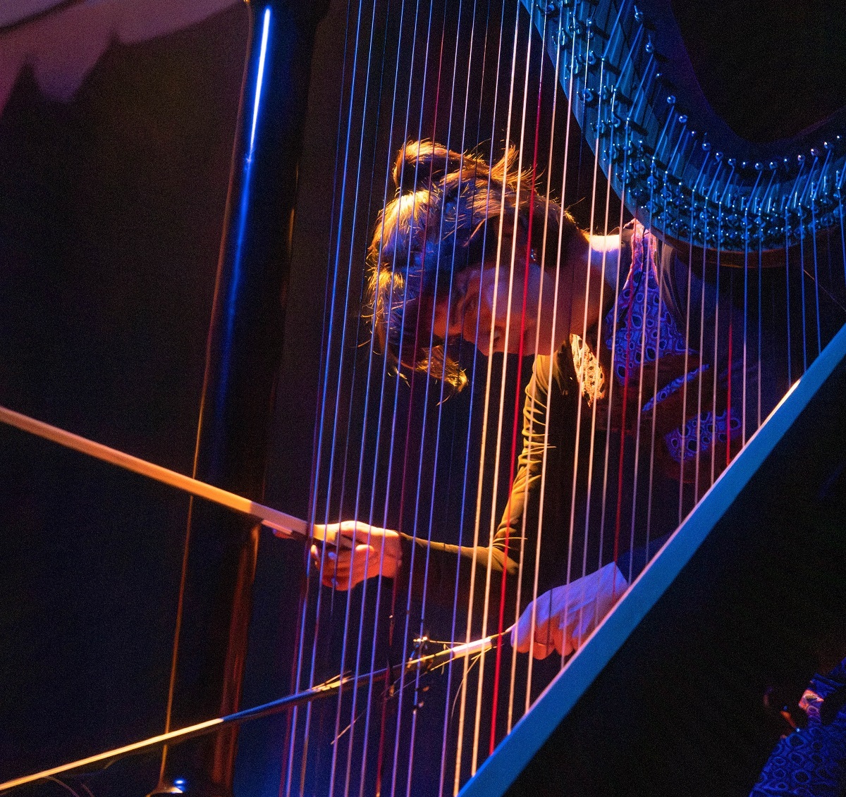 Foto von Marina Mello, die mit einem Bogen eine Harfe spielt