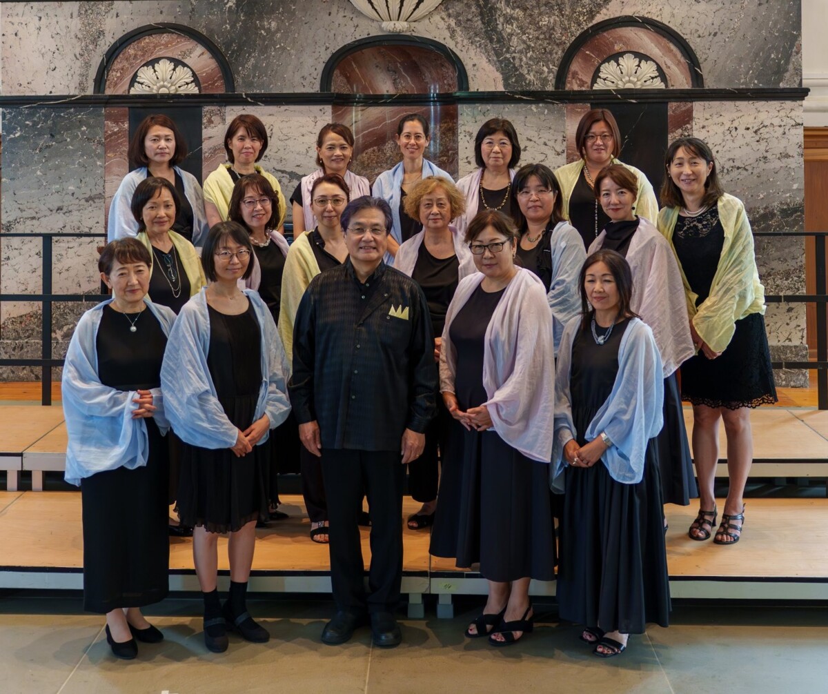 Bild des Nadeshiko Choirs, bestehend aus Frauen, die jeweils ein blaues, violettes oder gelbes Seidentuch umgehängt haben und dem Chorleiter
