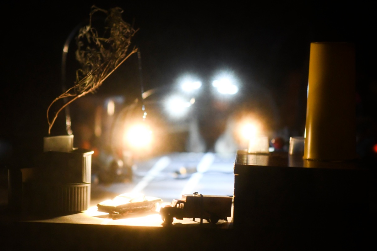 dunkler Raum mit Licht im Hintergrund, dass Gegenstände, wie ein Spielzeugauto, eine Kerze und eine Pflanze im Vordergrund anstrahlt