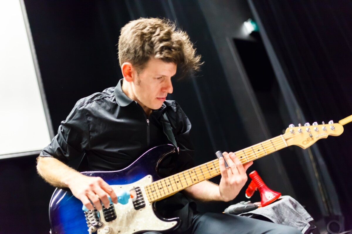 Foto Yaron Deutsch, der mit Slider in der einen Hand und einem kleinen Ventilator in der anderen Hand E-Gitarre spielt